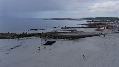 Drone-orbit-around-currach-boat-on-sandy-beach-canoes-at-gloomy-dawn-blueish-horizon