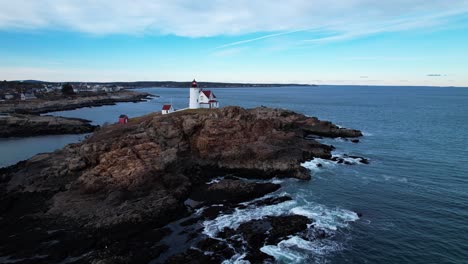 ascending angle of lighthouse on a rocky island with blue skies and water crashing on the rocks