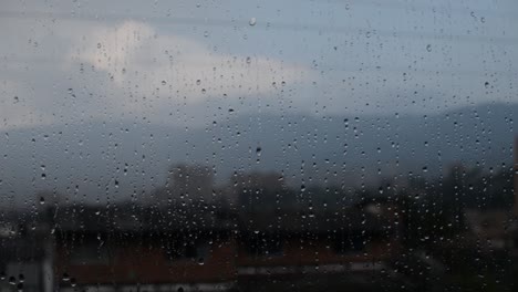 raindrops falling steadily through a window glass with the city in the background