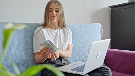 Junge-Frau-Sitzt-Fröhlich-Zu-Hause-Mit-Laptop-Und-Zählt-Geld