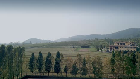 Italian-countryside-with-fields-and-tractor-harvesting-hay-near-a-farmhouse