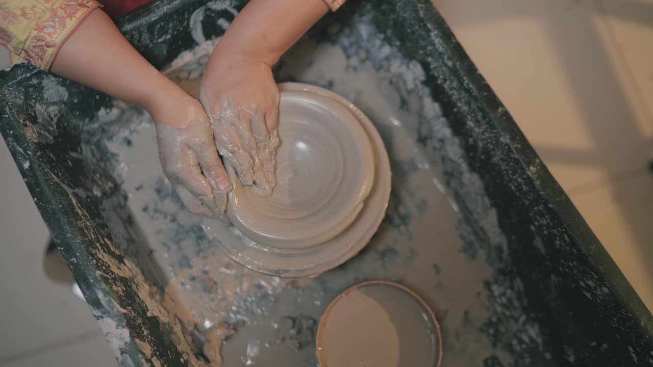 hands molding wet clay into a bowl on pottery wheel with natural light