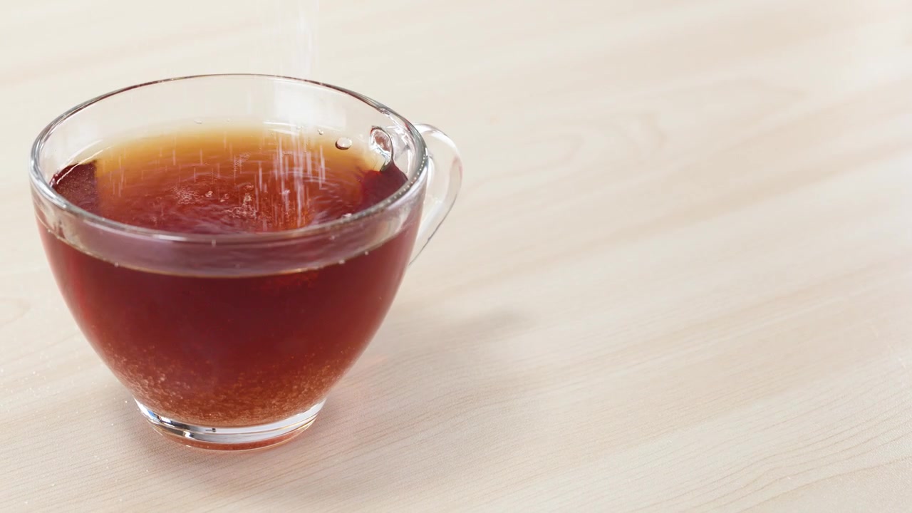 熱い紅茶が入った透明なガラスのカップに、グラニュー糖が注ぎ込まれる様子