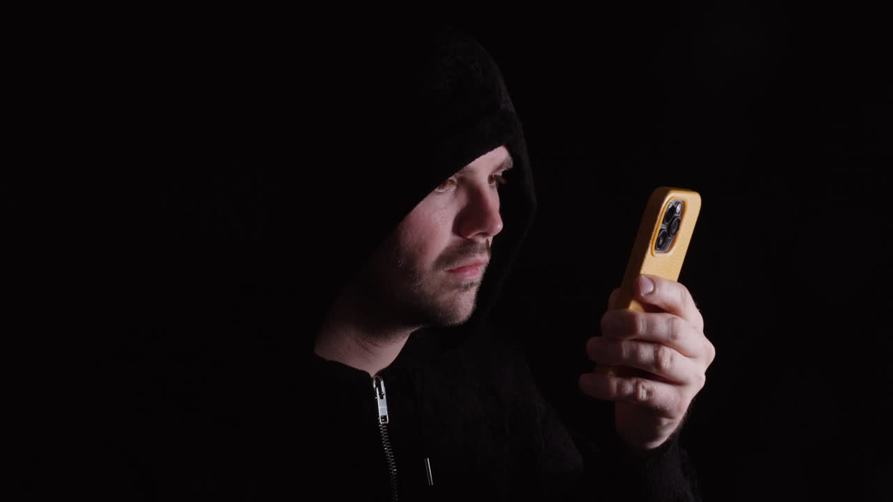 Uomo con una felpa scura con cappuccio che usa uno smartphone, rappresentando l'utilizzo dei social media, il comportamento digitale e l'interazione online