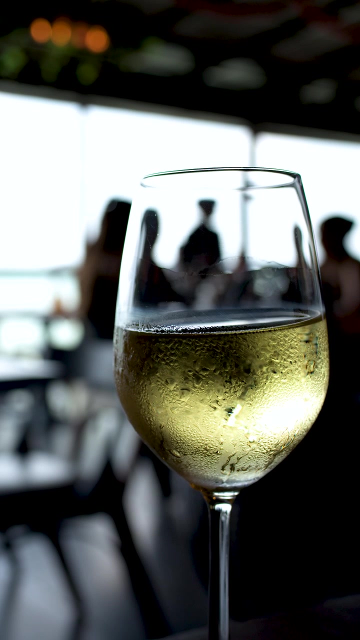 Un primo piano di un bicchiere di vino bianco freddo con condensa in un ristorante.