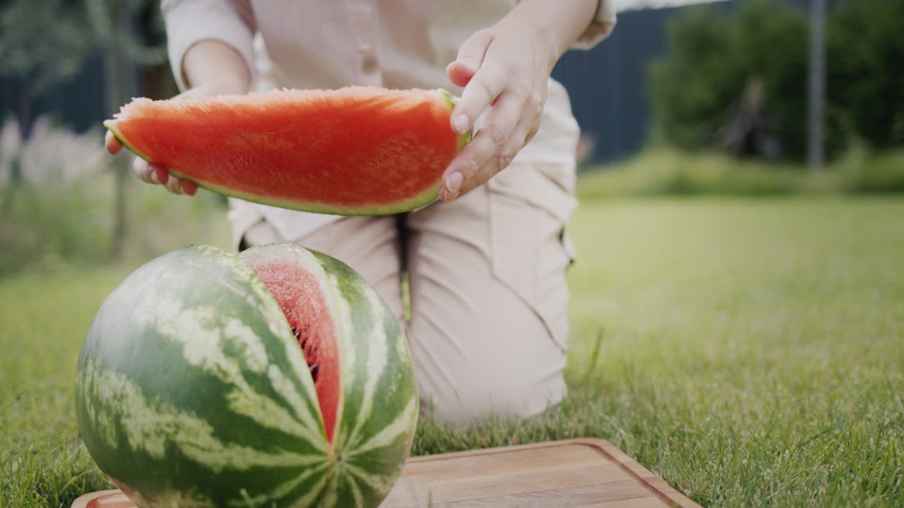 여자 가 피크닉 에서 수박 한 조각 을 자르고 있다