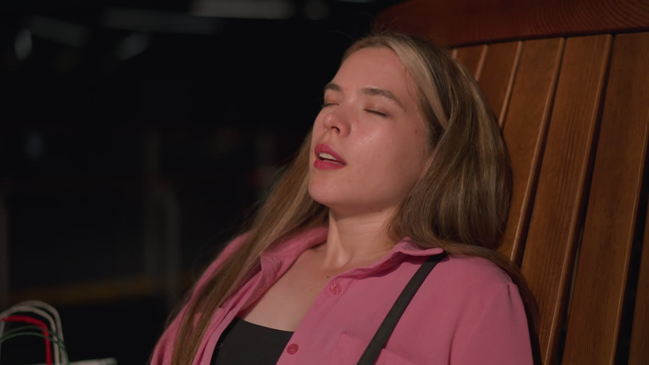 dama blanca en vestido rosa con bolso negro se sienta en un banco de madera marrón relajándose y tomando una respiración profunda, parte de las manijas de las bolsas de compras son visibles a su lado mientras disfruta de un momento de paz