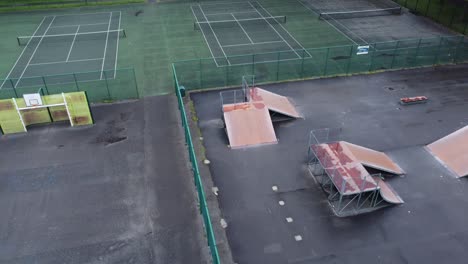 aerial view birdseye descent flying above fenced skate park ramp in empty closed playground