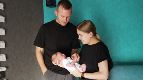beautiful caucasian couple with newborn. parents in black t-shirts waving their little baby.