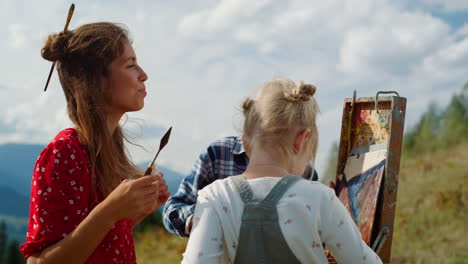 happy family creating picture outdoor. mother painting teaching kids in mountain