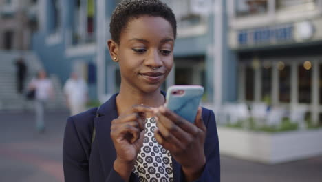 close up portrait of independent african american business woman smiling happy using smartphone texting browsing in city