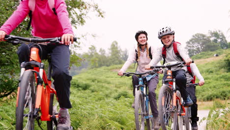 Parents-and-children-riding-mountain-bikes-on-a-country-path-during-a-family-camping-holiday,-Lake-District,-UK