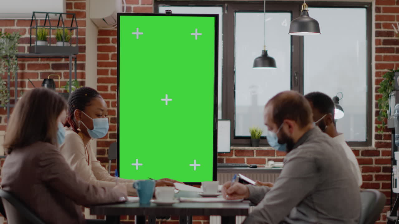 Poeple with face mask looking at monitor with green screen