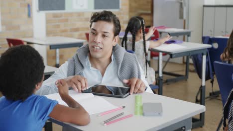 un maestro feliz y diverso que ayuda a los escolares a escribir en el aula de la escuela primaria