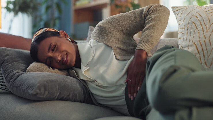 Woman experiencing abdominal pain on a couch