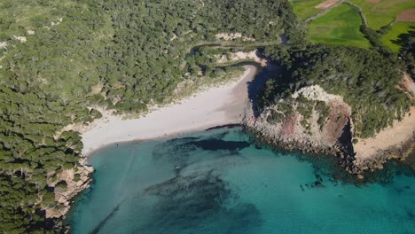 Cinematic-aerial-pan-around-white-sand-beach-along-the-coast-of-Menorca