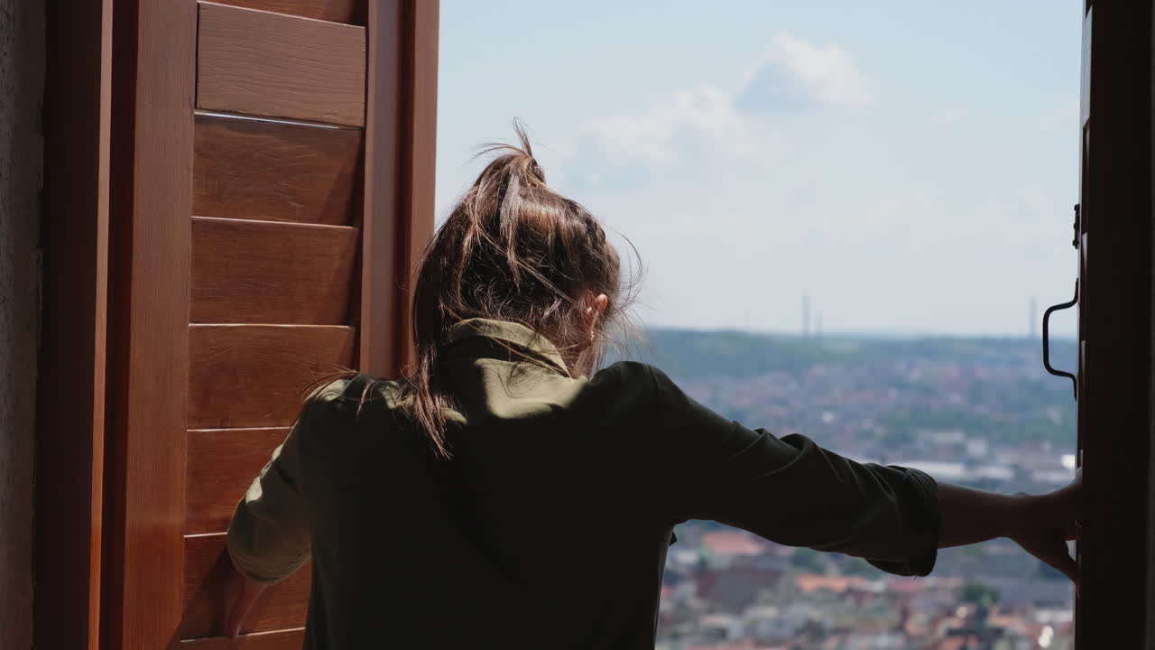 한 여자가 창문에서 시내를 바라보고 있다.