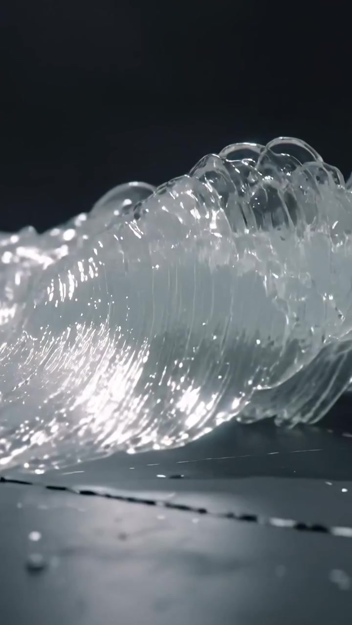 Video verticale: Un'onda che forma un velo di liquido trasparente che si muove su una superficie lucida, rilasciando goccioline.