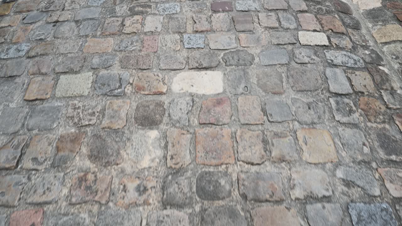 A low angle tracking shot moves across textured ancient stone pavement in daylight