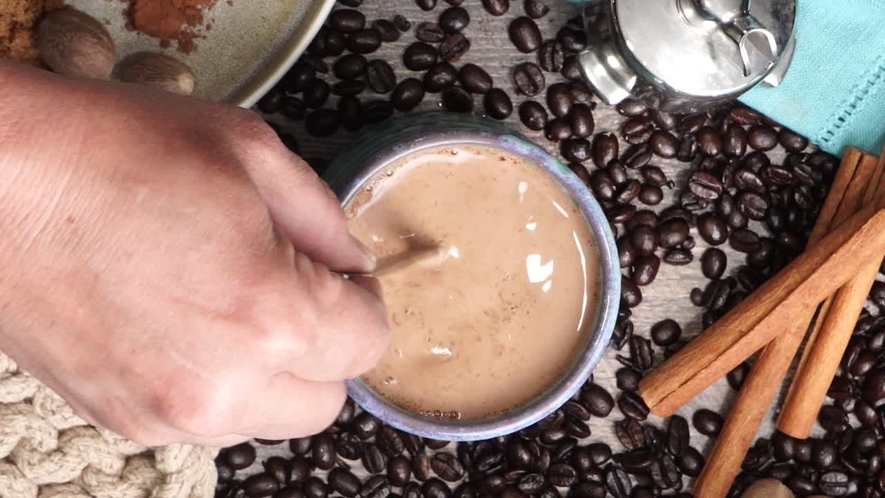 Cup or mug of coffee in a blue ceramic cup with whipped cream and a dash of nutmeg or cinnamon. Coffee beans surrounding a cozy cup of coffee in a blue mug.