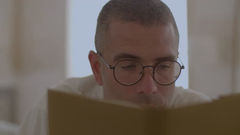 hombre caucásico enfocado leyendo un libro en la cama después de despertarse