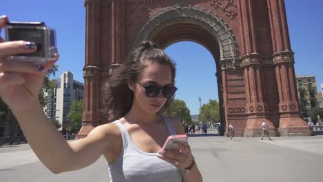 girl making video of herself on action camera. woman tourist near barcelona arch