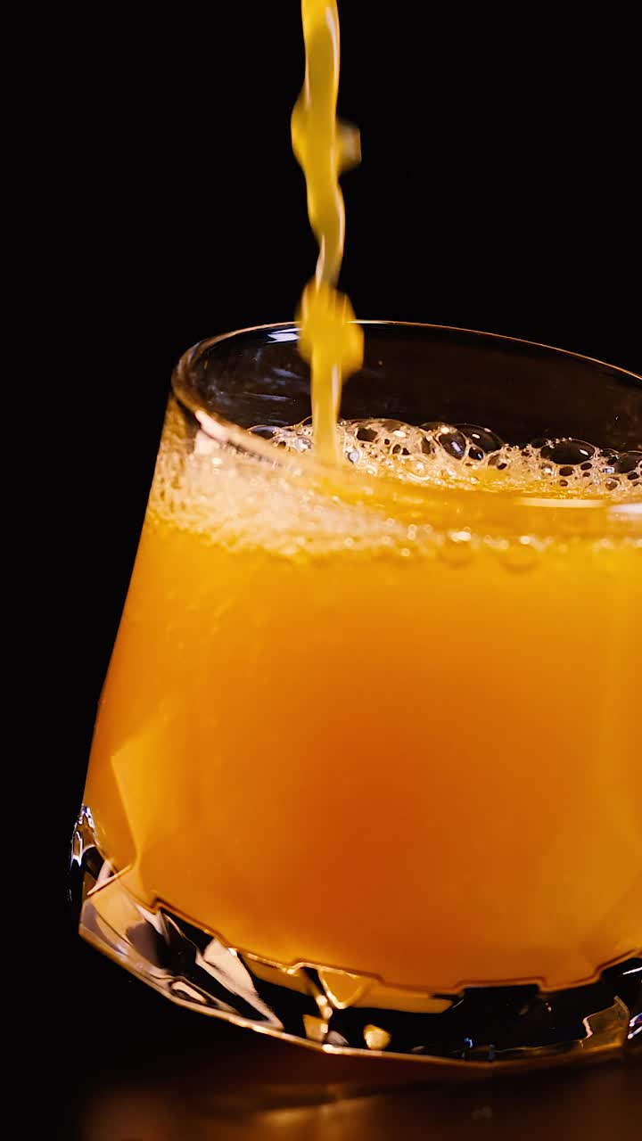 Un vivace getto di succo d'arancia riempie un bicchiere su uno sfondo scuro