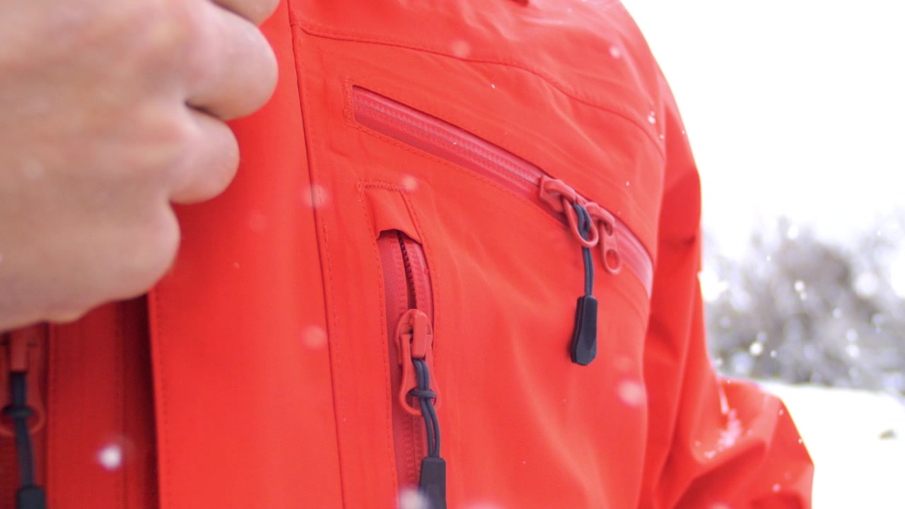 Person pulls zipper tab to open a red winter jacket while standing outdoors in the snow