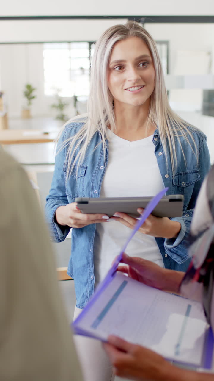 Vertical video of happy diverse business people with tablet talking in office
