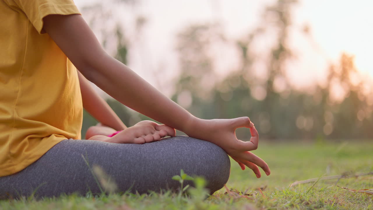 Close view of a woman’s hands resting on knees in Gyan Mudra while meditating outdoors, symbolizing peace, balance, and mindfulness