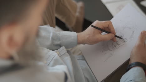 man is sketching a face of a person on a white paper with wooden pencil