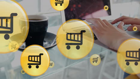 animación de iconos de carrito de compras, taza de café, manos recortadas de una mujer caucásica trabajando en una computadora portátil