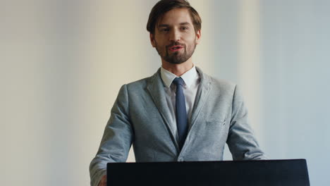 close-up view of caucasian businessman speaker on a podium wearing formal clothes and talking in a conference room in front to many people