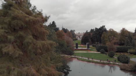 Drone-passing-trees-in-Sempione-Park,-Parco-Sempione,-Milan