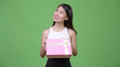 young beautiful asian businesswoman thinking while holding gift box