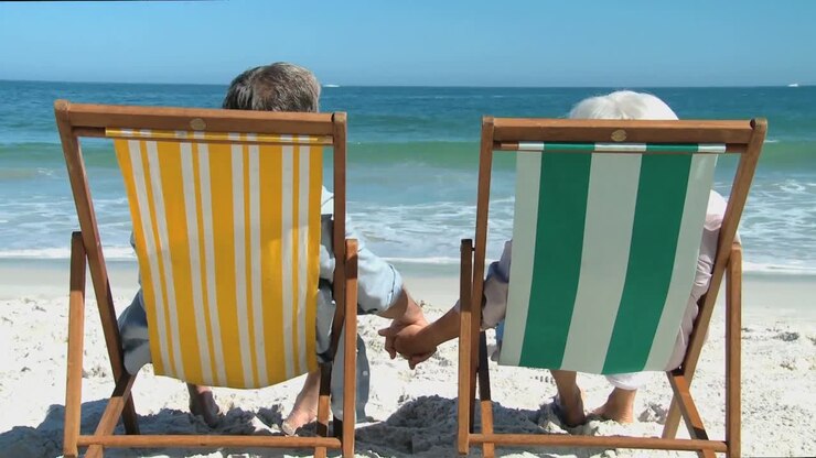 Ouder stel kijkt naar de oceaan, zittend op strandstoelen