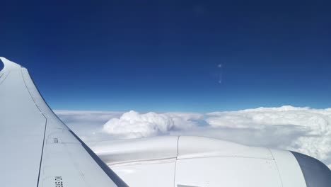 window seat view onto the plane's wing and engine above thick white clouds
