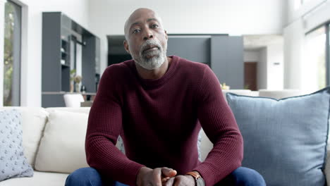 portrait of happy biracial man sitting on couch and having video call at home, slow motion