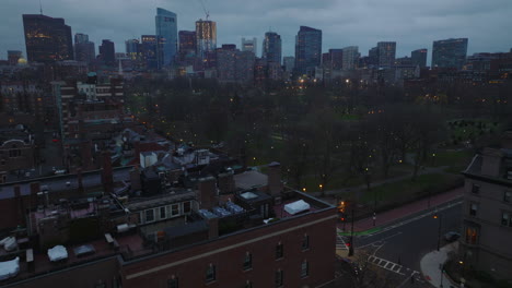 High-angle-view-of-cars-driving-on-road-along-park.-Tilt-up-reveal-cityscape-with-modern-high-rise-buildings-at-dusk.-Boston,-USA