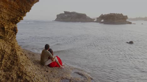 couple sitting on beach enjoying beautiful seascape, rocks formation in water