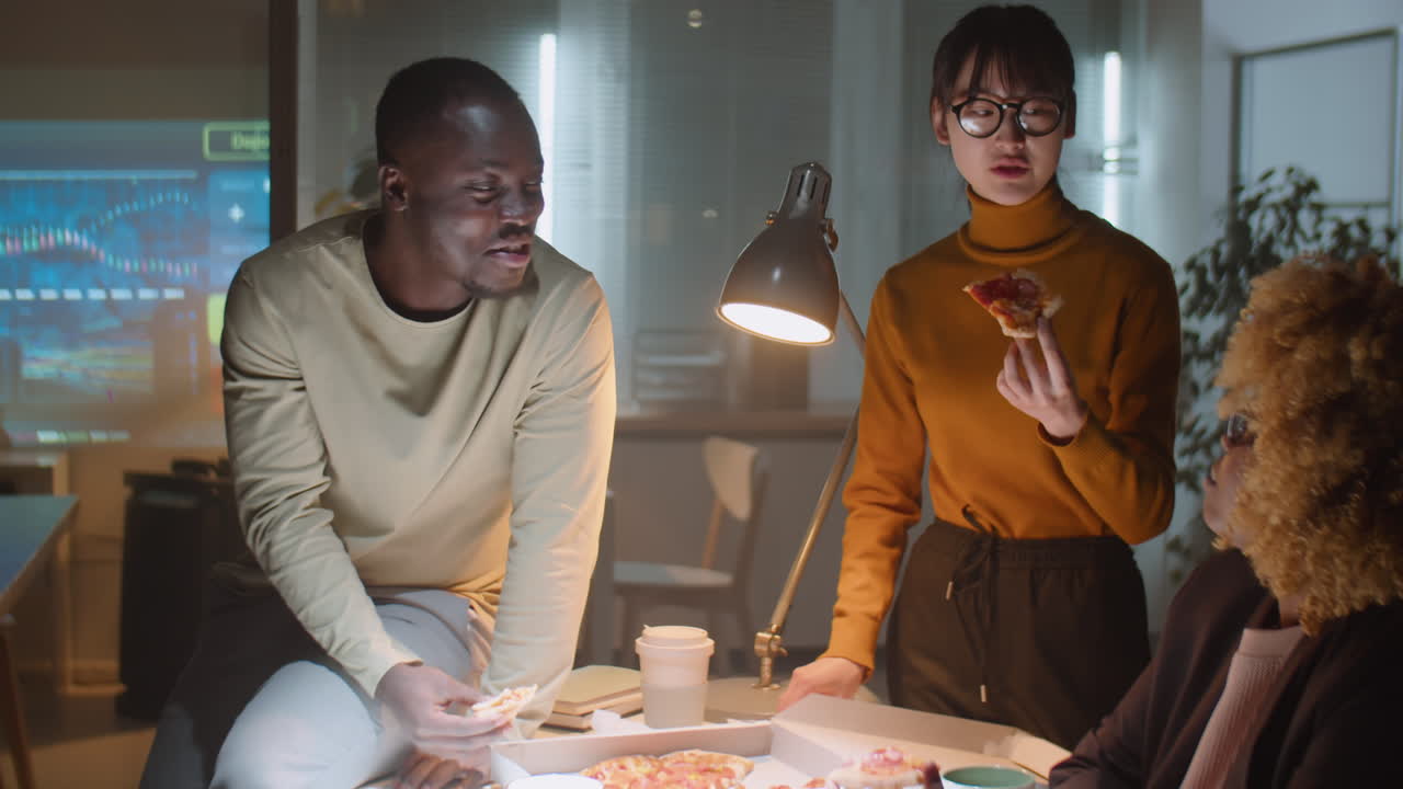 Diverse Business Team Eating Pizza and Talking in Office at Night