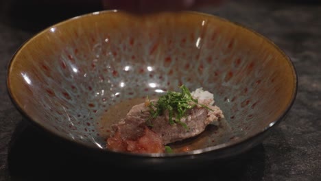 chefs makes plating of meat dish, adding bits of green veggies on top