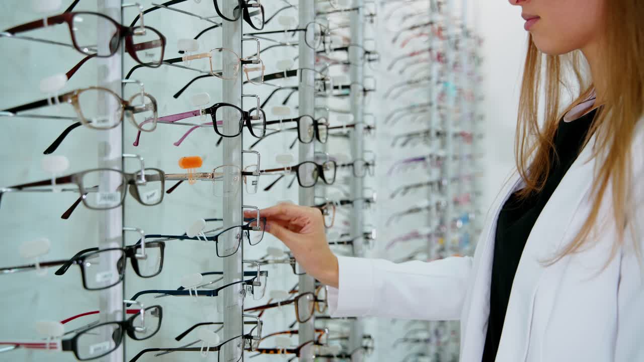 Eyeglasses on the stand in the optical store. Young buyer woman choosing fashionable spectacles. Eyewear concept.