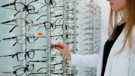 eyeglasses on the stand in the optical store. young buyer woman choosing fashionable spectacles. eyewear concept.