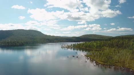 forward drone shot over a calm lake in finland with clouds reflected in it