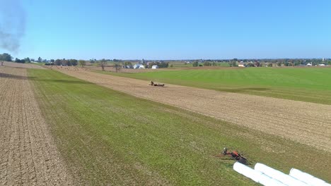 aerial view of an amish man and woman harvesting corn stalks and bailing in squares with horse drawn equipment on a sunny fall day