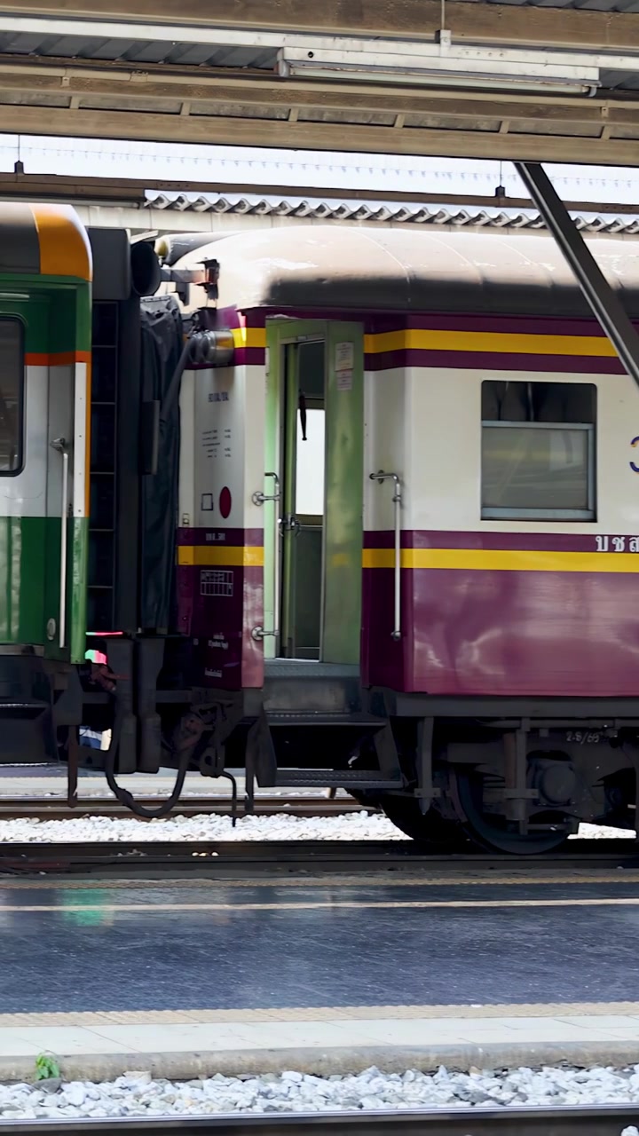 Vista laterale di un treno passeggeri d'epoca colorato che passa lentamente una banchina della stazione coperta di giorno.