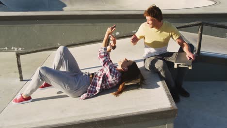 happy caucasian female and male friends using smartphone at a skatepark