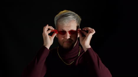 retrato de un joven seductor con ropa elegante de moda con gafas de sol rojas sobre fondo negro
