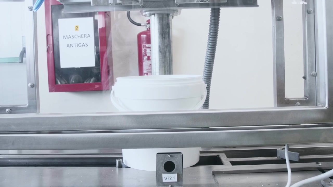A close-up of an industrial sealing machine pressing lids onto white plastic buckets during an automated food packaging process inside a clean manufacturing facility
